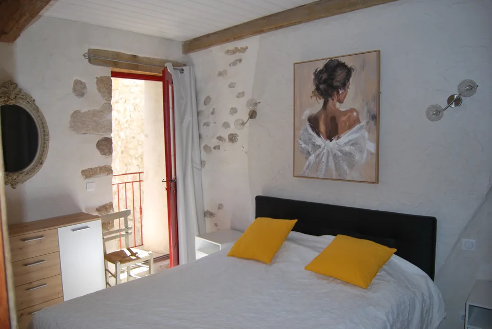 Double bedroom with yellow cushions, a painting, an old mirror and a door open onto the balcony