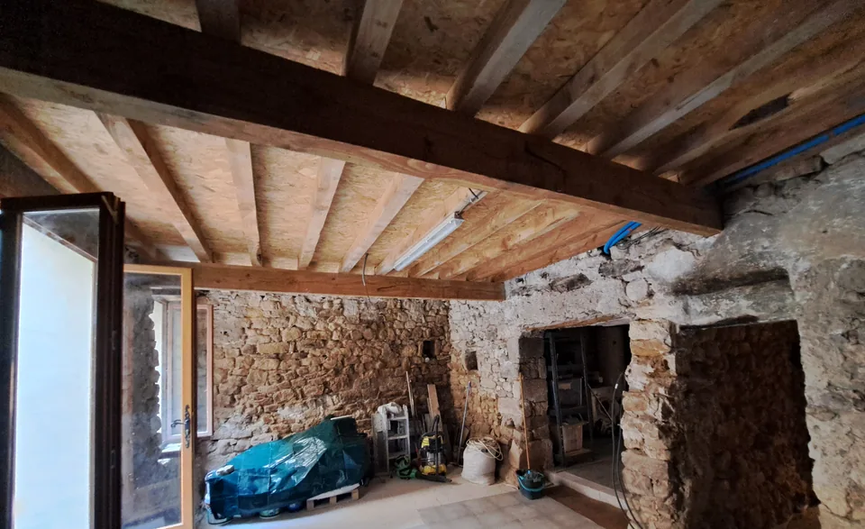 Outbuilding with new beams and exposed stone walls, opening onto the courtyard